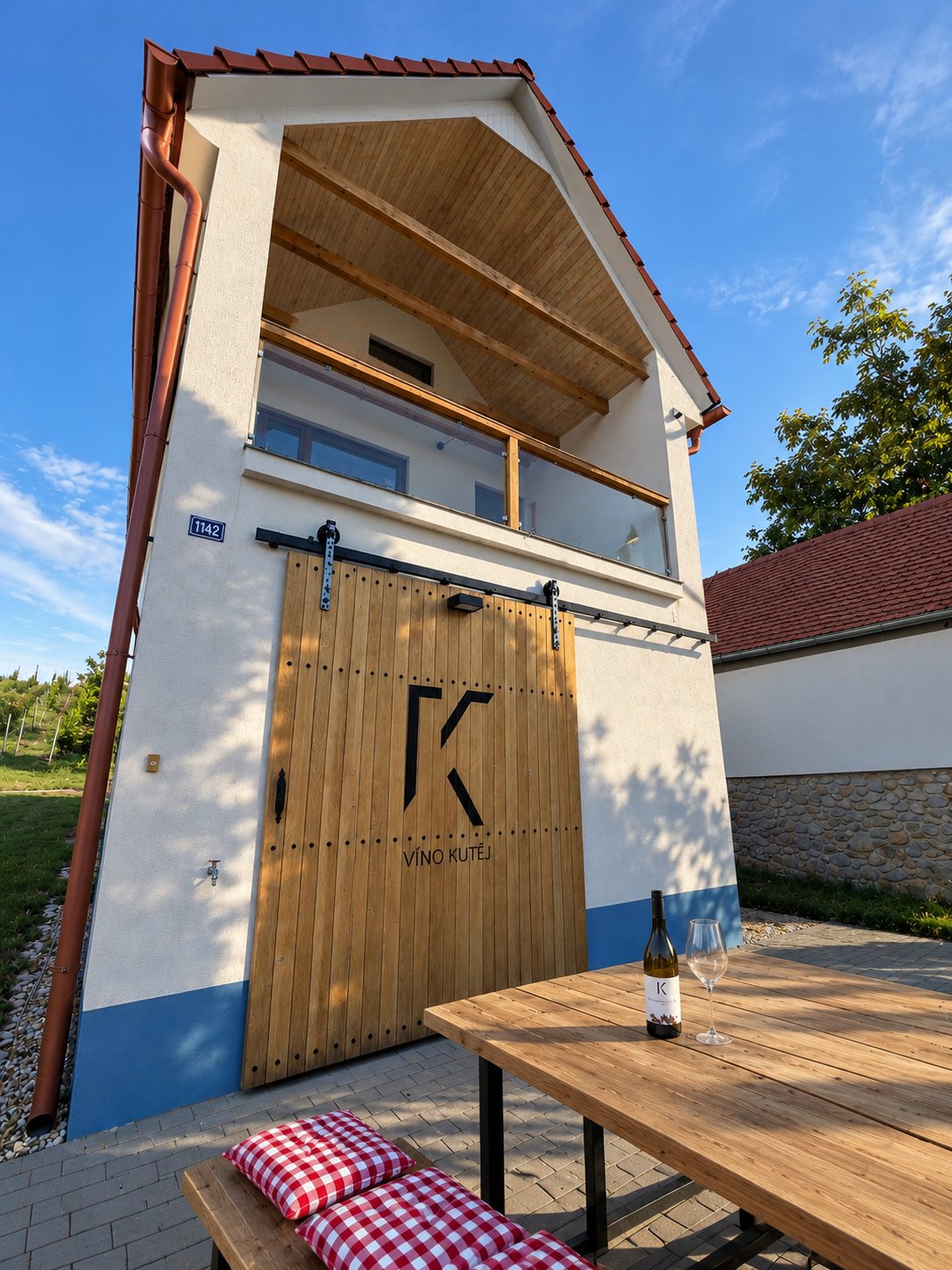 Vinařství Víno Kutěj – dům s bránou K a stolem s vínem před vinohradem